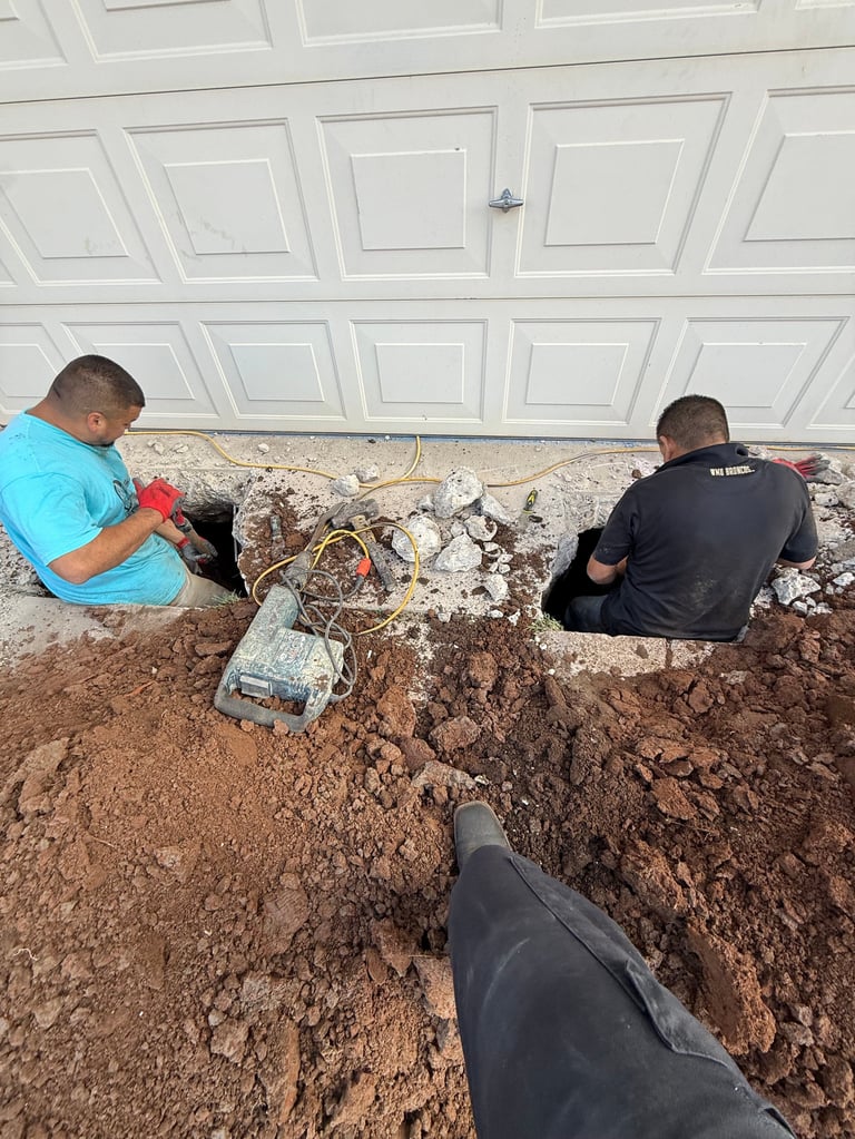 Two workers laying drainage pipe in excavated trench below a white garage door during underground installation project